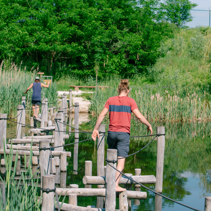 Twee mensen lopen over een houten palen brug over het water bij het blotevoetenpad
